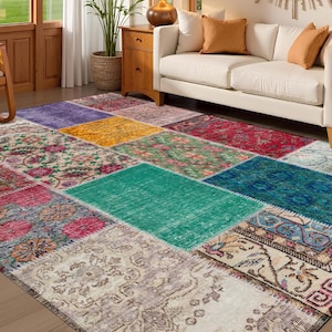 Op de afbeelding: Een patchwork tapijt met een verscheidenheid aan kleuren en patronen. Het tapijt heeft rechthoekige en vierkante patches in tinten rood, groen, blauw, geel en crème. Het tapijt ligt op een houten vloer in een woonkamer.