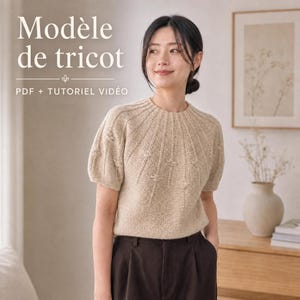 May include: A beige short-sleeved knit sweater with a round neckline and textured vertical ribbing radiating from the collar. The text "Modèle de tricot" and "PDF + TUTORIEL VIDÉO" is visible in the upper left corner of the image.