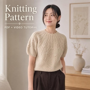 May include: A beige short-sleeved knit sweater with a round neckline and textured vertical stitch details radiating from the collar. The text Knitting Pattern PDF + VIDEO TUTORIAL is displayed in the upper left corner of the image.