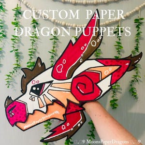 Puede incluir: Una marioneta de dragón de papel personalizada en rojo, blanco, marrón y naranja. La marioneta tiene un diseño detallado con el texto "CUSTOM PAPER DRAGON PUPPETS" y el nombre del artista, "MoonsPaperDragons".