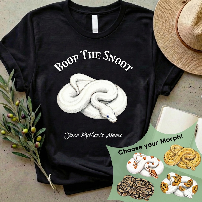 May include: Black t-shirt with the text "Boop the Snoot" above a white snake illustration. Below the snake is the text "Your Python's Name". A graphic shows different snake morphs. A straw hat and a notebook are in the background.