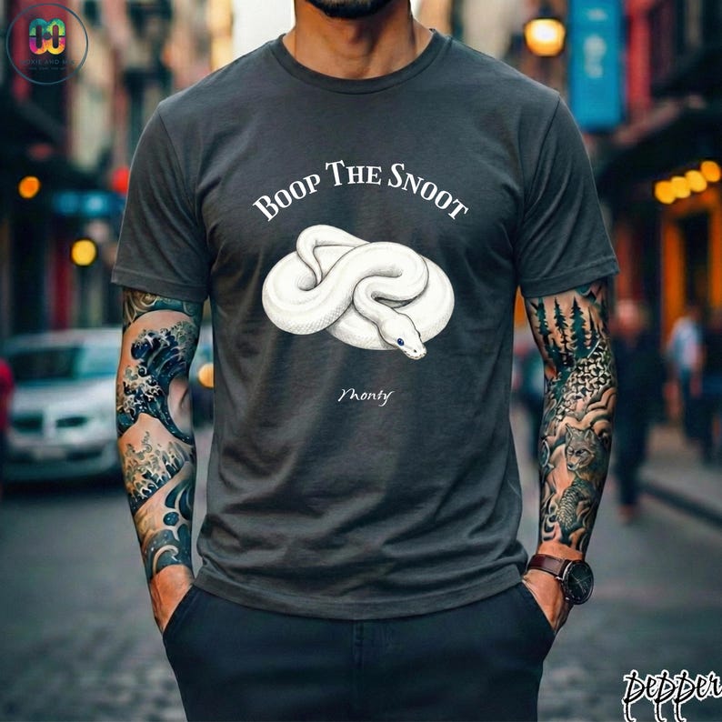 May include: Dark gray t-shirt featuring a white snake illustration with the text "Boop The Snoot" above and "Monty" below. The shirt is a crew neck style.