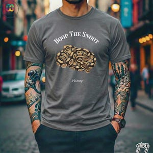 May include: A gray t-shirt with the text "Boop The Snoot" above a detailed illustration of a snake. The word "Monty" is below the snake illustration. The shirt is a solid color.
