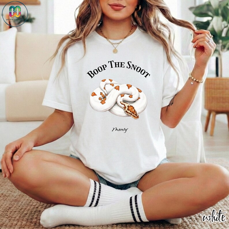 May include: White t-shirt featuring a graphic of a white and brown snake with the text "Boop The Snoot" above it and the name "Monty" below. The shirt also has the word "white" on the bottom right.