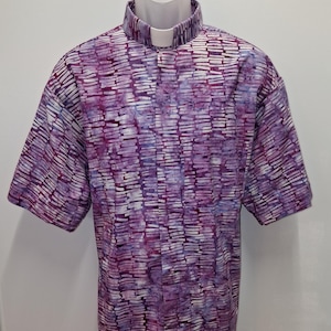 May include: A short-sleeved shirt with a white collar and a purple and white abstract pattern. The shirt is displayed on a white mannequin. The pattern is made up of horizontal and vertical lines.