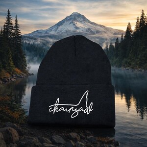 May include: A black knit beanie featuring a folded cuff and white embroidered text that reads "chainad" in a cursive script font. The beanie is constructed from a ribbed fabric material and displays the white lettering clearly on the front.
