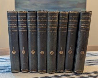 May include: A set of eight black hardcover books titled The Works of Charles Dickens, Household Edition. Each spine features gold lettering, the text Illustrated by Darley & Gilbert, and a circular Boz emblem near the bottom edge of the book.