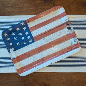 May include: Rectangular serving tray with a distressed American flag design. The tray features red and white stripes, a blue corner with white stars, and cut-out handles. The text "WARREN KIMBLE" is printed on the tray.