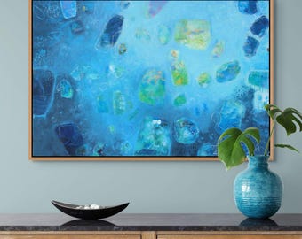 May include: Abstract art print in a wooden frame. The artwork features a blue and turquoise colour palette with various shapes and forms. The painting is displayed above a wooden cabinet with a black decorative bowl and a blue vase.