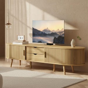 May include: A light wood TV stand with a slatted design, two drawers, and two cabinet doors. A flat-screen TV displays a mountain landscape. A small vase and a decorative calendar sit on top of the stand.