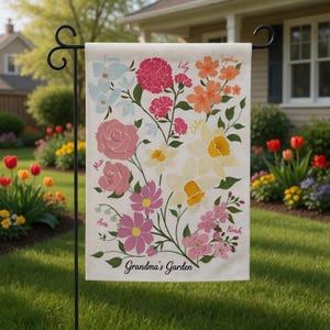 Puede incluir: Una bandera de jardín con un diseño floral en tonos rosa, naranja, amarillo y azul. La bandera incluye nombres como Emma, Lily y Sophia, con el texto "Grandma's Garden" en la parte inferior, en un soporte de metal negro.