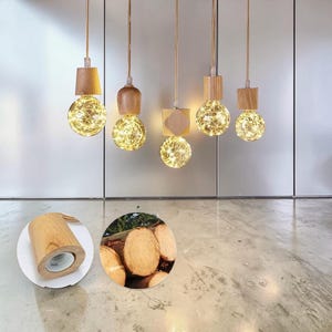 May include: Five hanging pendant lights with light-coloured wooden fixtures and spherical glass bulbs containing glowing, thin wire fairy lights. The wooden components vary in shape, including cylindrical, rounded, and square designs.