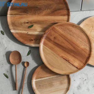 Puede incluir: Un conjunto de fuentes y cucharas de madera. Las fuentes son redondas con un acabado natural de vetas de madera, algunas con un diseño de dos tonos. También hay dos cucharas de madera de diferentes tamaños, todo dispuesto sobre una superficie gris claro.