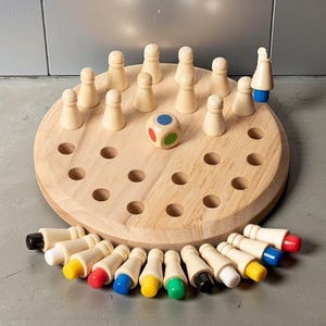 May include: Wooden board game with a circular wooden base, featuring small wooden pegs and a colorful die. The game includes a set of colored pegs, each with a different colored top. A classic strategy game for all ages.