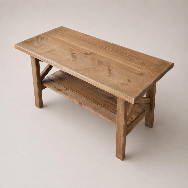 K&ouml;nnte beinhalten: Eine rechteckige Holzbank mit nat&uuml;rlicher hellbrauner Oberfl&auml;che, bestehend aus einer flachen Tischplatte, vier stabilen Beinen und einer unteren Ablage. Das Design zeigt sichtbare Holzmaserungen und Kreuzstreben an den Seiten des Gestells.