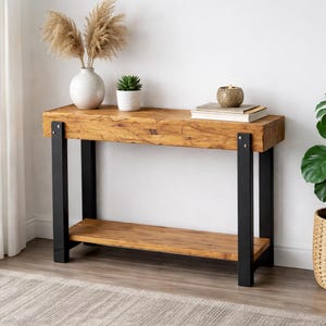 Könnte beinhalten: Rustikaler Konsolentisch aus Naturholz mit schwarzen Metallbeinen. Der Tisch hat eine untere Ablage und ist mit dekorativen Gegenständen wie einer Vase und Büchern geschmückt. Die Tischlänge beträgt ca. 120 cm.