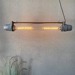 May include: A hanging industrial-style light fixture. The fixture features a clear glass tube with two exposed filament bulbs. The ends are encased in gray metal fixtures, and it is suspended by chains.