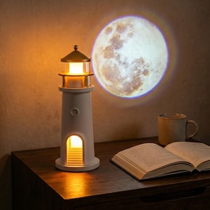 Pode incluir: Uma lâmpada branca em forma de farol que emite uma luz quente e projeta uma imagem da lua na parede. Uma caneca e um livro aberto repousam sobre uma superfície de madeira escura, criando um ambiente acolhedor.