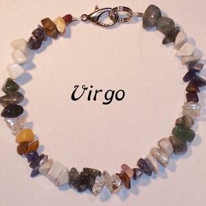 May include: A Virgo gemstone bracelet featuring a variety of colorful, irregularly shaped stones. The stones are in shades of white, green, brown, purple, and clear. The bracelet is secured with a silver-colored clasp. The word "Virgo" is written in black script.