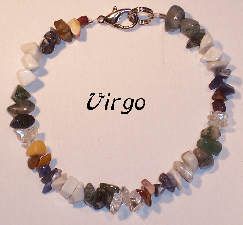 May include: A Virgo gemstone bracelet featuring a variety of colorful, irregularly shaped stones. The stones are in shades of white, green, brown, purple, and clear. The bracelet is secured with a silver-colored clasp. The word "Virgo" is written in black script.