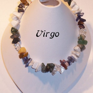 May include: A colorful gemstone bracelet with a variety of stone shapes and colors, including white, green, purple, and clear stones. The bracelet is displayed on a white stand, with the word "Virgo" in black script.