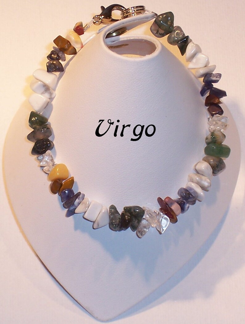 May include: A colorful gemstone bracelet with a variety of stone shapes and colors, including white, green, purple, and clear stones. The bracelet is displayed on a white stand, with the word "Virgo" in black script.