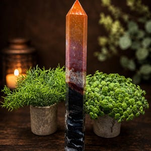 May include: A tall, multi-colored crystal tower with a pointed top. The stone features a vertical color gradient transitioning from a bright orange at the apex, through shades of deep red and brown, down to a solid, textured black base.
