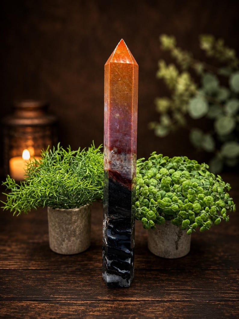 May include: A tall, multi-colored crystal tower with a pointed top. The stone features a vertical color gradient transitioning from a bright orange at the apex, through shades of deep red and brown, down to a solid, textured black base.