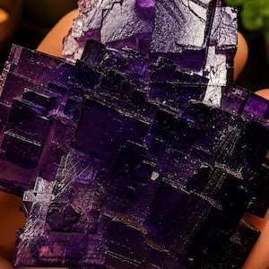 Pode incluir: Um grupo de cristais de fluorite roxo profundo com forma&ccedil;&otilde;es geom&eacute;tricas c&uacute;bicas n&iacute;tidas. O esp&eacute;cime mineral apresenta camadas transl&uacute;cidas e facetas angulares complexas com intensidades variadas de tons violeta e roxo escuro.
