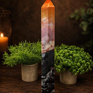 May include: A tall, hexagonal crystal tower featuring a distinct color gradient. The top section is a vibrant orange and red, transitioning into a dark, opaque black base with white veining throughout the stone's polished, smooth surface.