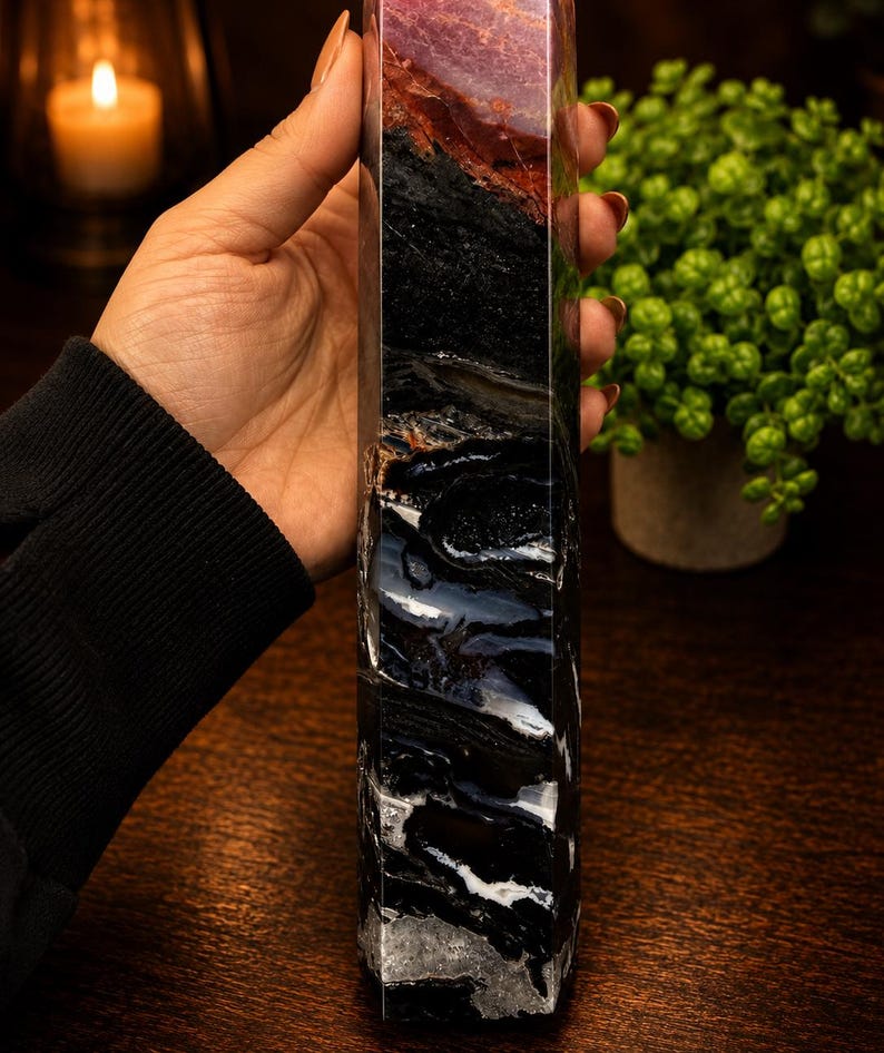 May include: A tall, multi-faceted stone tower featuring a distinct color gradient. The top section displays a deep reddish-brown hue, transitioning into a solid black middle, and ending in a base with intricate black and white banded agate patterns.