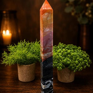 May include: A tall, multi-colored stone tower with a pointed, faceted top. The upper section features warm tones of orange, yellow, and pink, while the lower section transitions into a dark, solid black base with white, marbled, and textured patterns.