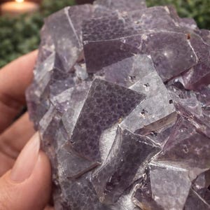 Peut inclure: Gros plan sur un amas de cristaux de fluorite violette. Le cristal a une structure cubique avec un m&eacute;lange de teintes violet clair et fonc&eacute;. La surface a un aspect textur&eacute;, avec des formations cristallines visibles.
