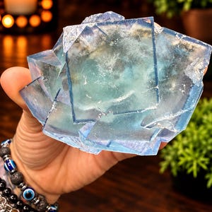 May include: A large, translucent blue fluorite crystal cluster featuring distinct cubic formations. The mineral displays varying shades of light to deep blue with internal cloudy inclusions and sharp, geometric edges throughout the specimen.