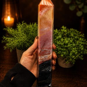 May include: A tall, polished crystal tower featuring a multi-colored gradient. The stone transitions from a deep black base through layers of dark red and earthy brown, ending in a lighter, translucent orange-toned point at the top.