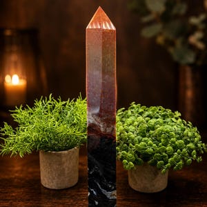 May include: A tall, six-sided crystal tower with a pointed top. The stone features a gradient of colors, transitioning from a translucent orange at the apex to a deep, opaque black with white veining at the base, showcasing a smooth, polished finish.