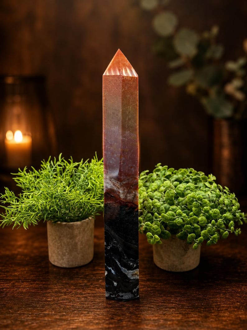 May include: A tall, six-sided crystal tower with a pointed top. The stone features a gradient of colors, transitioning from a translucent orange at the apex to a deep, opaque black with white veining at the base, showcasing a smooth, polished finish.