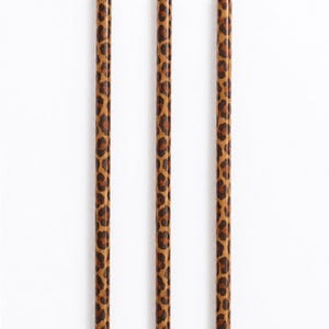 May include: Three cylindrical drinking straws arranged vertically, each featuring a repeating brown and black leopard print pattern against a tan background. The straws are uniform in shape and length, displaying a consistent animal-inspired design.