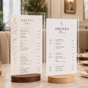 May include: Two vertical rectangular acrylic signs displaying a drinks menu with black text and botanical illustrations. Each sign is supported by a semi-circular wooden base, one in a dark walnut finish and the other in a light oak finish.