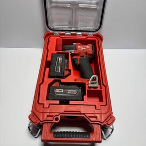 May include: A red Milwaukee Packout tool case containing a red and black M18 cordless impact driver, two M18 Redlithium XC5.0 batteries, and a metal belt clip. The clear lid features the Milwaukee logo and the word Packout.