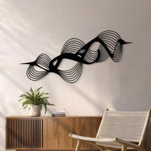 May include: Black metal wall art with a flowing, abstract design. The artwork features curved lines and shapes, creating a dynamic and modern aesthetic. The piece is mounted on a neutral-colored wall, complementing the room's decor.