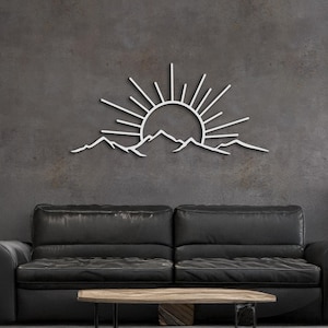 Pu&ograve; includere: Opera d'arte da parete in metallo bianco raffigurante un'alba su una catena montuosa. L'opera &egrave; montata su una parete grigio scuro, sopra un divano in pelle nera e un tavolino in legno. Design minimalista e moderno.