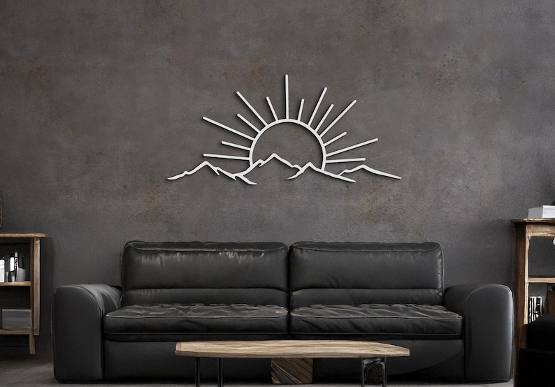 Pu&ograve; includere: Opera d'arte da parete in metallo bianco raffigurante un'alba su una catena montuosa. L'opera &egrave; montata su una parete grigio scuro, sopra un divano in pelle nera e un tavolino in legno. Design minimalista e moderno.