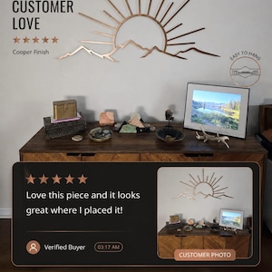 Pu&ograve; includere: Opera d'arte da parete in metallo color rame raffigurante un sole che sorge sulle montagne. L'opera &egrave; montata su una parete bianca sopra un mobile in legno. Il testo "Real Customer Love" e "Easy to Hang" &egrave; incluso.