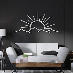 Pu&ograve; includere: Opera d'arte da parete in metallo bianco raffigurante un'alba su una catena montuosa. L'opera &egrave; montata su una parete grigio scuro sopra un divano bianco. I raggi del sole si estendono verso l'esterno, creando una silhouette suggestiva.