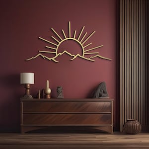 Pu&ograve; includere: Un'opera d'arte da parete in metallo color oro raffigurante un'alba su una catena montuosa. I raggi del sole si estendono verso l'alto e le montagne sono dettagliate con picchi e valli. L'opera &egrave; montata su una parete bordeaux.