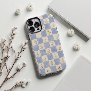Könnte beinhalten: Eine Smartphone-Hülle mit einem hellblauen und cremefarbenen Karomuster. Jedes Quadrat enthält eine kleine, zarte Illustration verschiedener Wildblumen, darunter Gänseblümchen und Klee, in sanften Grün-, Rosa- und Weißtönen.