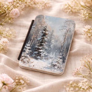 May include: A rectangular case with a winter landscape painting. The artwork depicts snow-covered trees in a forest, rendered in shades of blue, gray, and white. The case has a black spine and is surrounded by flowers.