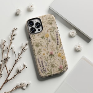 May include: A smartphone case featuring a detailed, textured print of wildflowers including white Queen Anne's lace, yellow buttercups, purple lavender, and pink clover on a cream-colored background, with a black camera lens cutout.