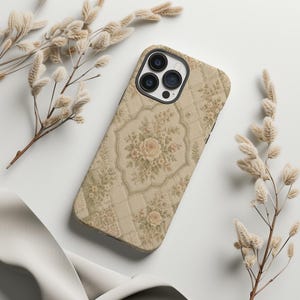 May include: A smartphone case featuring a beige quilted pattern with a repeating floral design of soft pink roses and green leaves. The case has a black camera cutout area with three circular lenses and a flash, covering the back of the device.